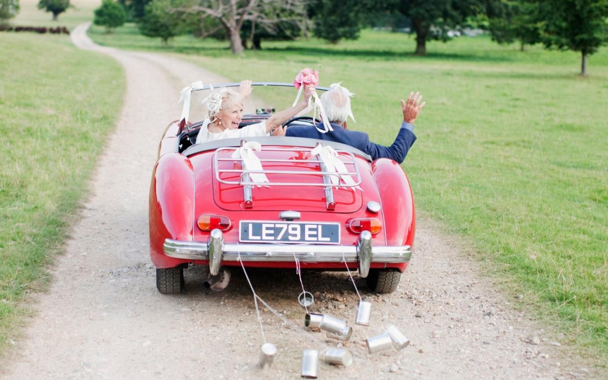 Bride and groom waving as they drive off in  convertible classic car - Ojo Images