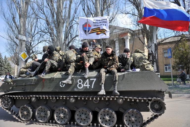 Men wearing military fatigues sit by a Russian flag and a white flag reading "People's volunteer corps of Donetsk" as they ride on an armoured personnel carrier (APC) in the eastern Ukrainian city of Slavyansk, on April 16, 2014
