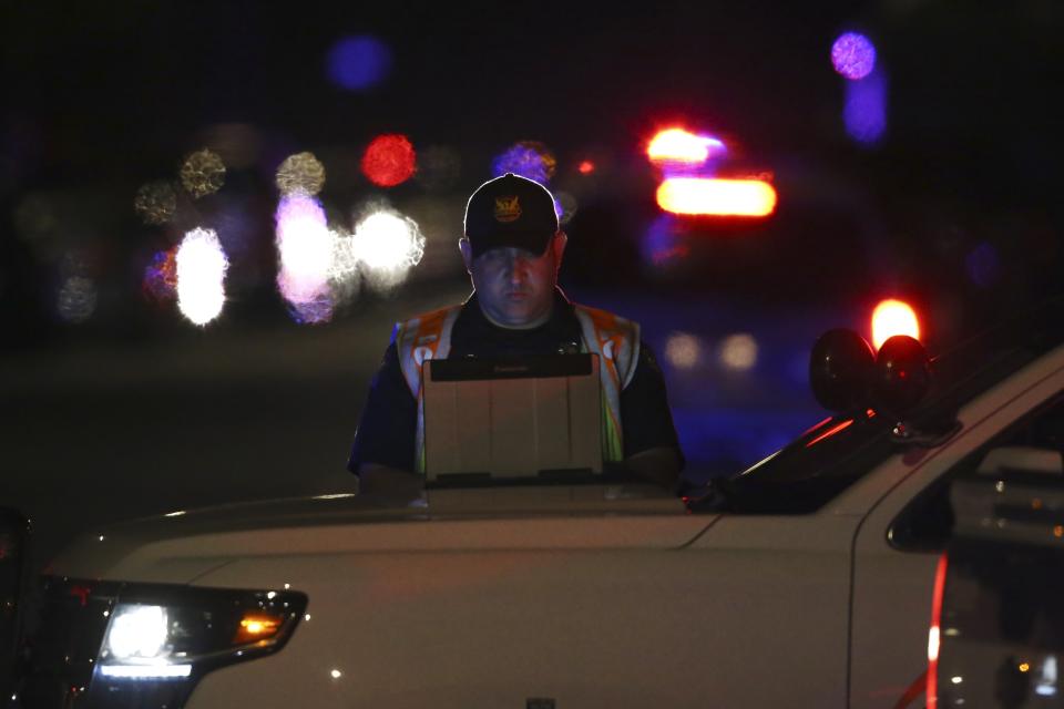 A Phoenix Police officer works on his computer near the scene of a deadly shooting in Phoenix, Ariz., Sunday, March 29, 2020. At least three Phoenix police officers were shot Sunday night on the city's north side, authorities said. (AP Photo/Ross D. Franklin)