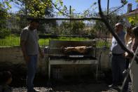 The Easter lamb is spit-roasted as Alexandros Ehrmann, left, smiles to his son Giorgos-Filippos and Christina Anastasopoulou, right, holds her daughter Amelia next to her father Giorgos, in Myrodafni village, Epirus region, northwestern Greece, on Sunday, April 24, 2022. For the first time in three years, Greeks were able to celebrate Easter without the restrictions made necessary by the coronavirus pandemic. (AP Photo/Thanassis Stavrakis)