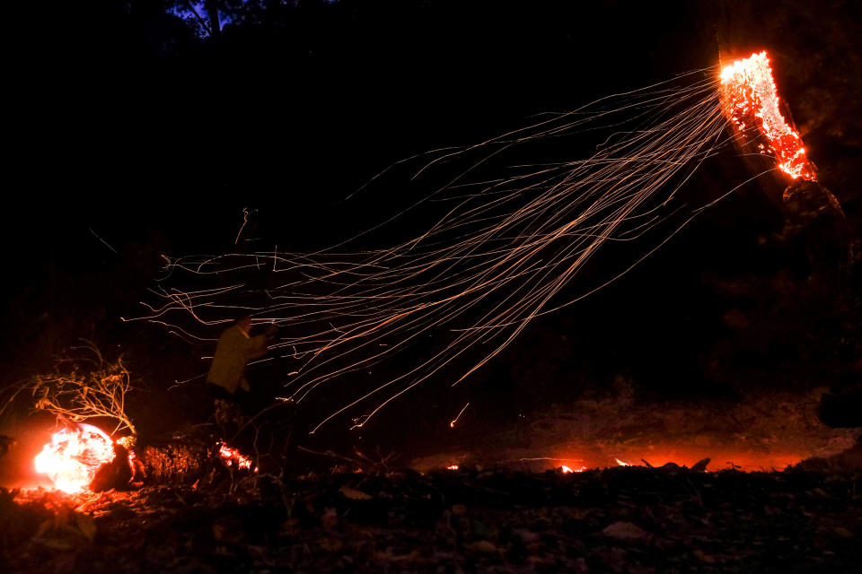 A photographer takes photos as wind whips embers from a tree burned by a wildfire Wednesday, Oct. 13, 2021, in Goleta, Calif. (AP Photo/Ringo H.W. Chiu)