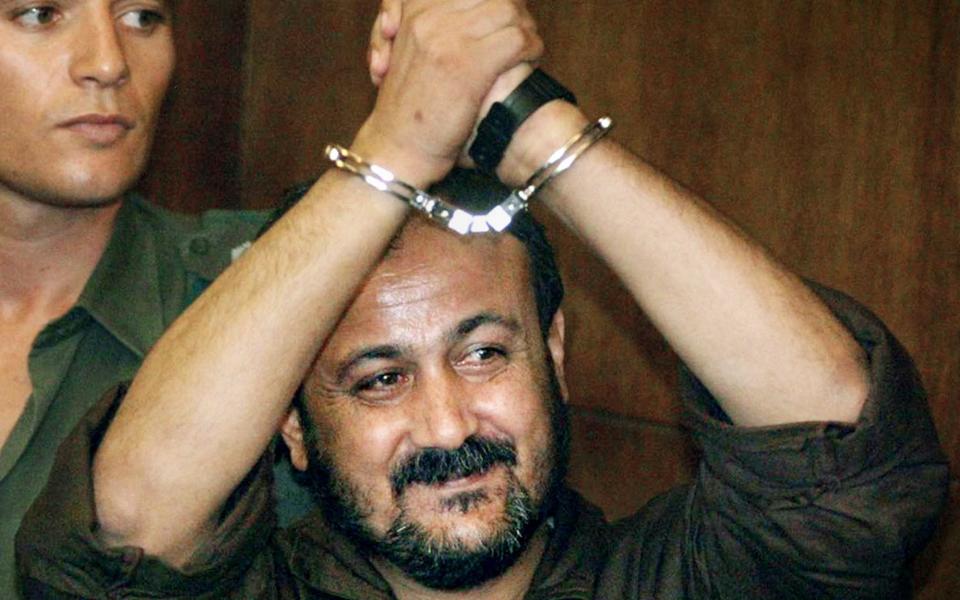 Jailed Palestinian uprising leader Marwan Barghouti raises his handcuffed hands as he enters the courtroom for the opening day of his trial at Tel Aviv's, Israel, District Court, in this file photo taken Aug. 14, 2002.  - Credit: AP