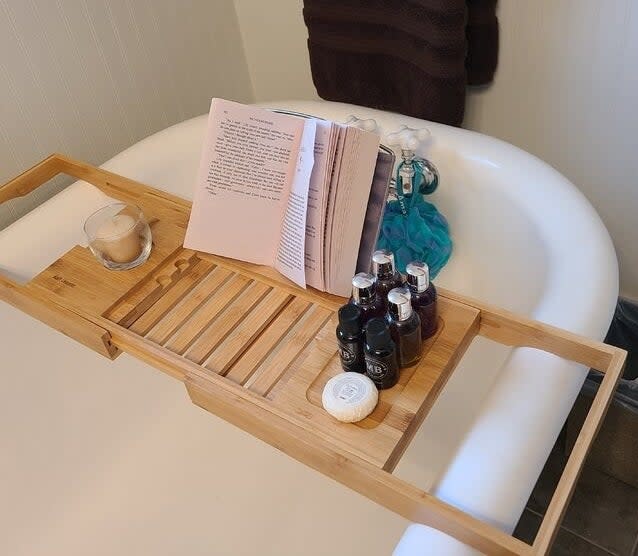 reviewer photo of the caddy on a tub with a book and bath supplies on it