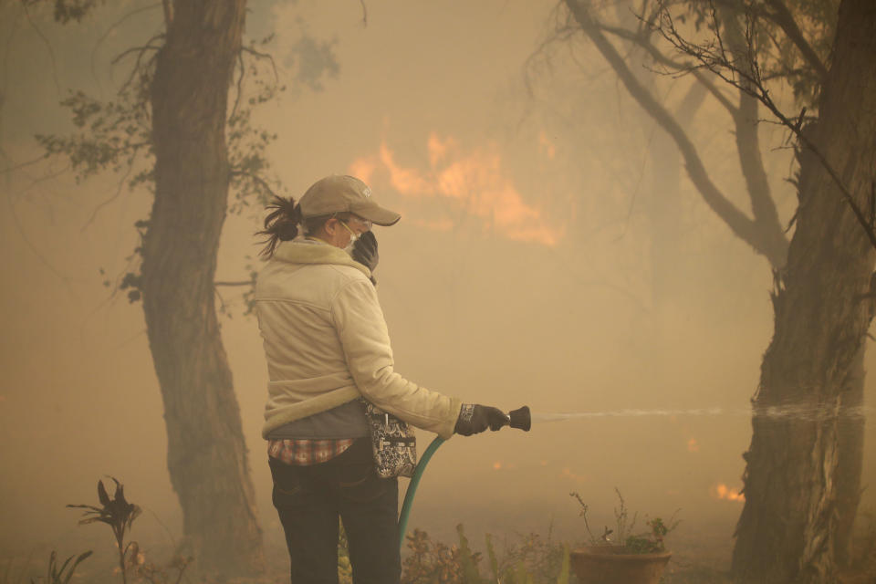 Beth Rivera hoses down her property as the Easy fire approaches Wednesday, Oct. 30, 2019, in Simi Valley, Calif. Driven by powerful Santa Ana winds, the brush fire broke out before dawn between the cities of Simi Valley and Moorpark north of Los Angeles and exploded to more than 1,300 acres (526 hectares), threatening 6,500 homes, Ventura County officials said. (AP Photo/Marcio Jose Sanchez)