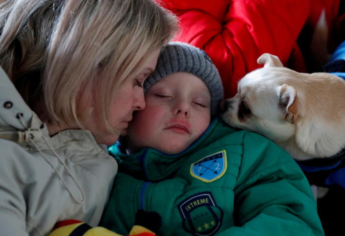 A woman comforts her child as a dog looks on. 