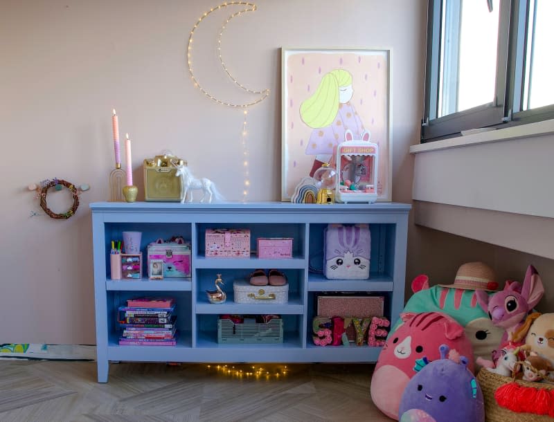 Side hutch holds stacked books, items in child's pastel bedroom.