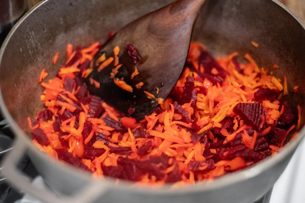 A wooden spoon stirs shredded cabbage and beets in a large pot.