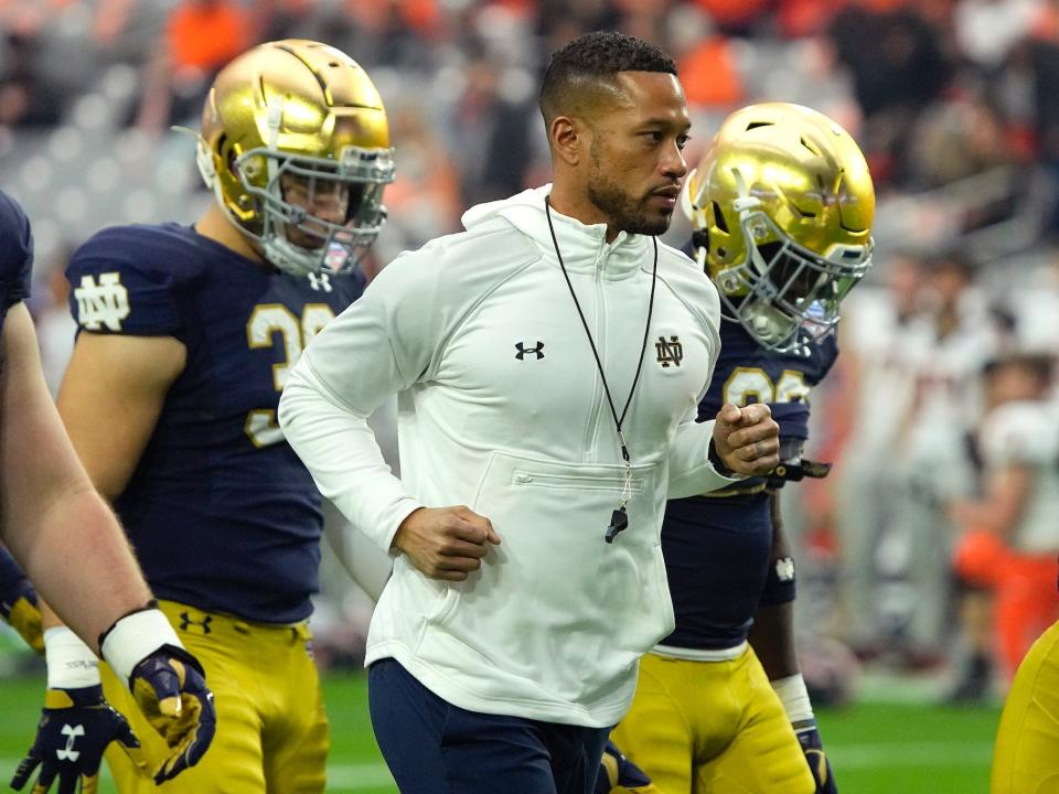 Marcus Freeman jogs onto the field surrounded by two other Notre Dame players.