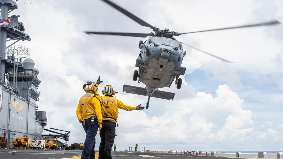 Sailors aboard the amphibious assault ship Essex signal to an MH-60S Sea Hawk helicopter with Helicopter Sea Combat Squadron (HSC) 21 during a replenishment-at-sea, Aug. 30, 2021. (Marine Corps)