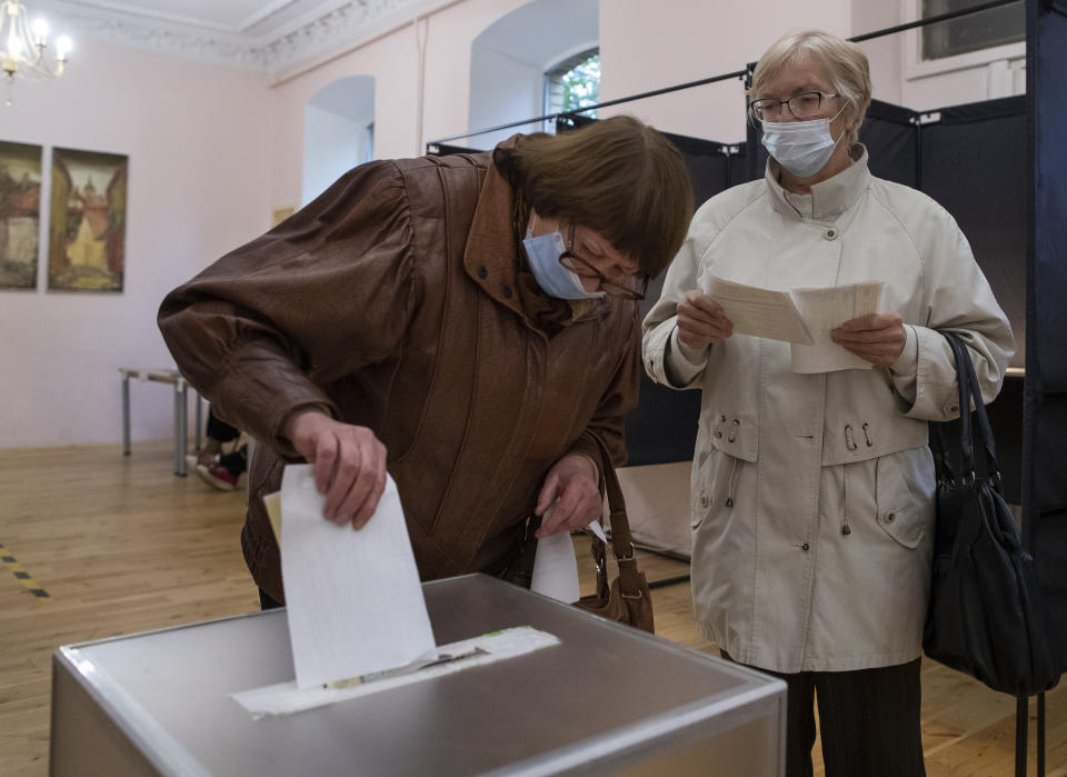 A Lithuanian woman, wearing face masks to protect against coronavirus cast their ballots at a polling station during parliamentary elections in Vilnius, Lithuania, Sunday, Oct. 11, 2020. Polls opened Sunday for the first round of national election in Lithuania, where voters will renew the 141-seat parliament and the ruling four-party coalition is widely expected to face a stiff challenge from the opposition to remain in office. (AP Photo/Mindaugas Kulbis)