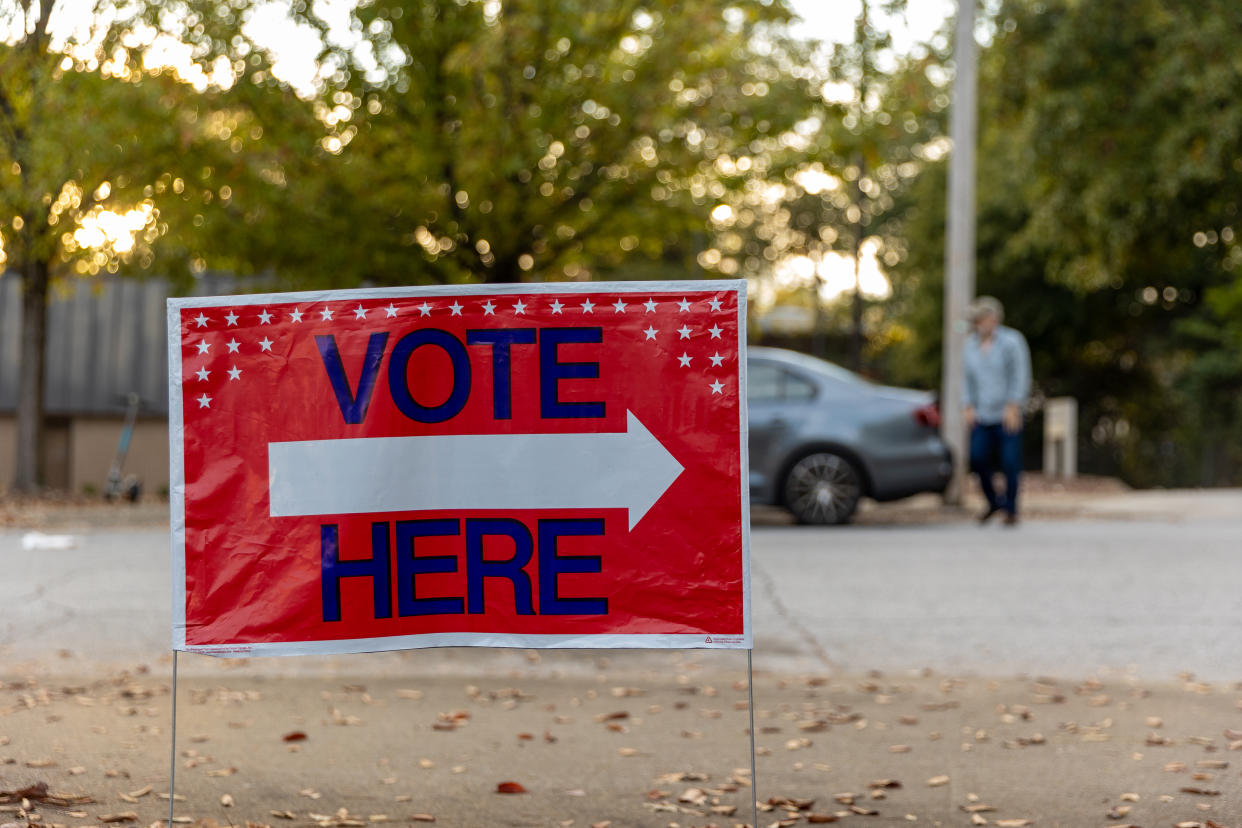 A sign with an arrow on a tree-lined street reads: Vote Here.