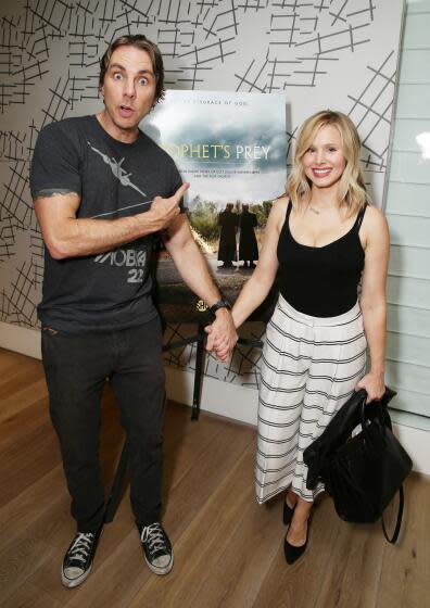 Dax Shepard and Kristen Bell posing in front of a film poster while holding hands.