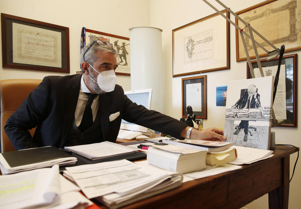 Luca Fusco, president of Facebook group "We Will Denounce" touches a painting which shows his father, in Brusaporto, near Bergamo, Italy, Thursday, March 18, 2021. Bergamo’s state-of-the-art Pope John XXIII Hospital verged on collapse last March: as army trucks ferried virus dead from the city’s over-taxed crematoria, doctors struggled to care for 600 COVID patients, 100 in intensive care. One year later, the picture is much improved: the hospital now is treating fewer than 200 virus patients, just one quarter of those requiring intensive care. (AP Photo/Antonio Calanni)