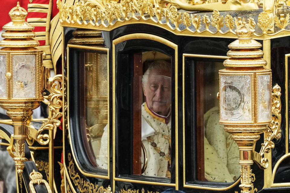 El rey Carlos III de Inglaterra, visto a través de la ventanilla del carruaje Jubileo de Diamante a su salida del Palacio de Buckingham, acompañado por la reina consorte, Camila, para la ceremonia de su coronación, en Londres, el 6 de mayo de 2023. (AP Foto/Frank Augstein)