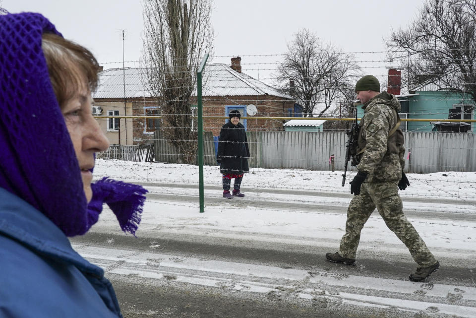 Ukrainian Valentina Boldyreva, left, tries to speak to her sister Raisa Yakovleva, center, who stands behind barbed wire on the Russian side of the Russia-Ukraine border as a Ukrainian border guard patrols an area in Milove town, eastern Ukraine, Sunday, Dec. 2, 2018. Valentina Boldyreva stepped out of her two-storey house on an overcast and snowy December afternoon to say hello to her 76-year-old sister who lives on the other side of Friendship of People's Street, a three-meter barbed-wire fence separating Russia from Ukraine and separating these sisters from each other. (AP Photo/Evgeniy Maloletka)