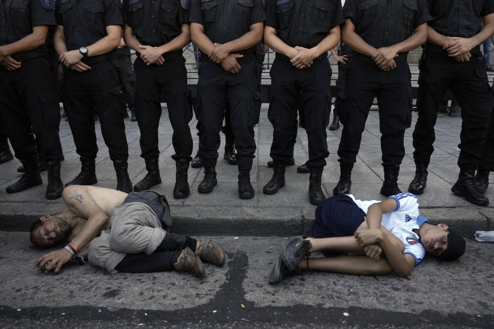 Police form a cordon on the perimeters of Congress as Cristian Rojas, who is homeless, and 14-year-old student Alejandro Imhoff lie before them in a fetal position, during a demonstration as part of a national strike to protest the economic and labor reforms proposed by Argentine President Javier Milei, in Buenos Aires, Argentina, Wednesday, Jan. 24, 2024. (AP Photo/Rodrigo Abd)