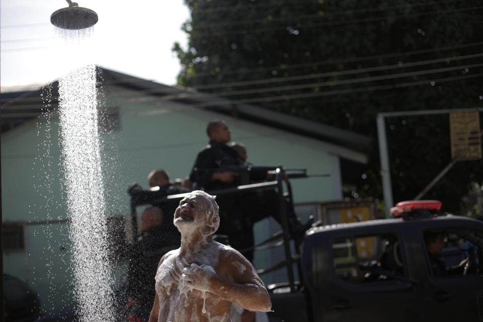 A man takes a shower as policemen patrol during an operation at the Mare slums complex in Rio de Janeiro, March 30, 2014. Federal troops and police occupied the Mare slums complex on Sunday to help quell a surge in violent crime following attacks by drug traffickers on police posts in three slums on the north side of the city, government officials said. Less than three months before Rio welcomes tens of thousands of foreign soccer fans for the World Cup, the attacks cast new doubts on government efforts to expel gangs from slums using a strong police presence. The city will host the Olympics in 2016. REUTERS/Ricardo Moraes (BRAZIL - Tags: CRIME LAW SOCIETY SPORT SOCCER)