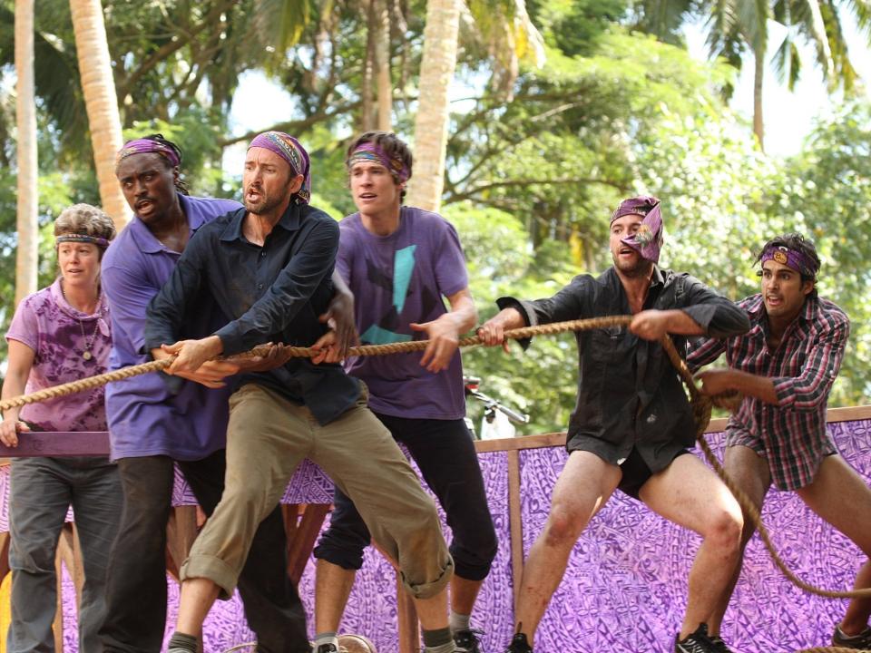 Survivor players wearing purple tugging on a rope during a challenge