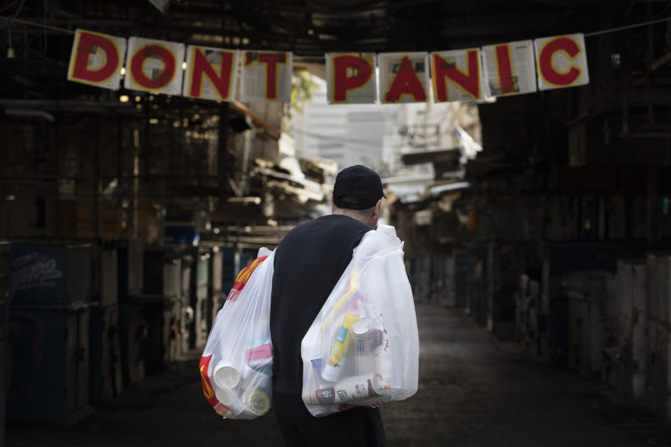 A man carries his shopping as he walks by a "don't panic" sign hanging at the entrance of a food market that is closed in order to reduce the spread of the coronavirus, in Tel Aviv, Israel, Monday, March 23, 2020. In Israel daily life has largely shut down with coronavirus cases multiplying greatly over the past week. (AP Photo/Oded Balilty)