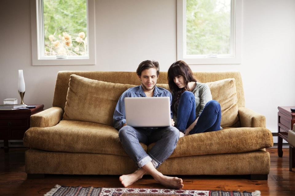 man using laptop computer while sitting with girlfriend on sofa at home
