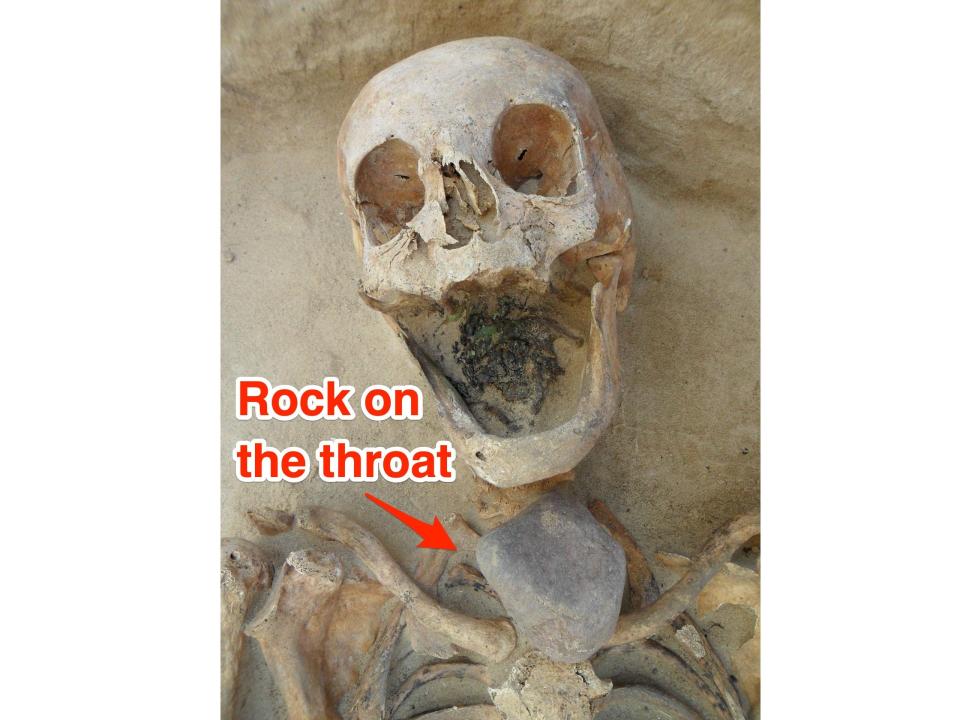 A skeleton is shown in situ with no teeth and a rock under the chin