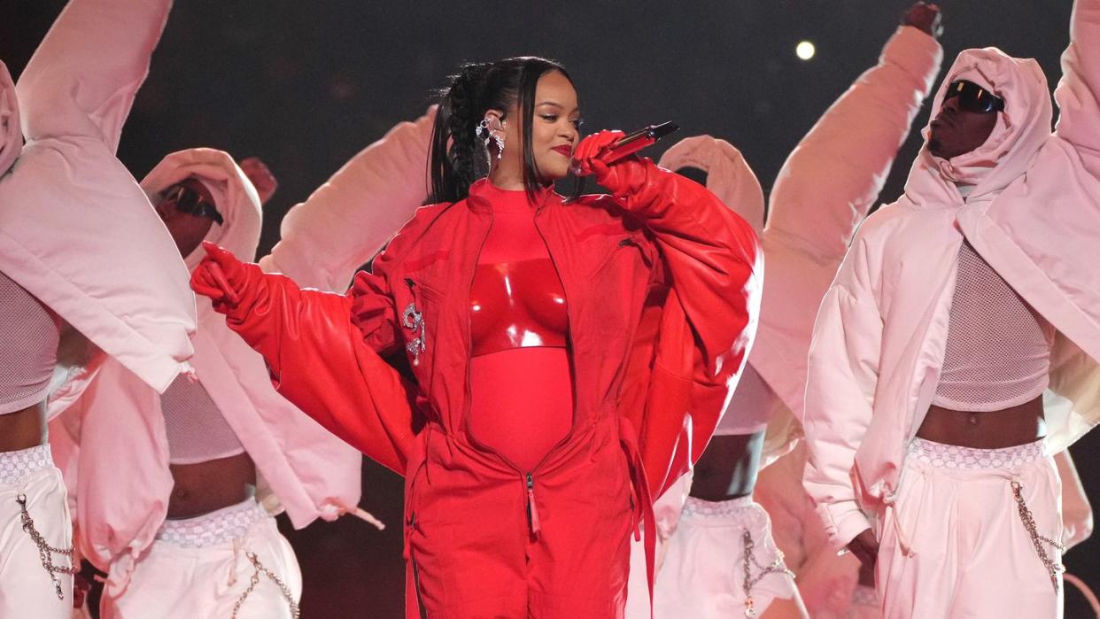 rihanna wearing a red outfit while singing into a microphone in front of several dancers wearing all white