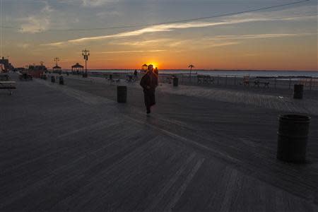 People walk on the Coney Island boardwalk as the sun peaks over the horizon in the Brooklyn borough of New York City, October 28, 2013. REUTERS/Brendan McDermid