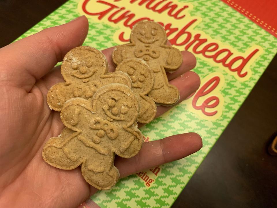 hand holding cookies of trader joes mini gingerbread people in front of green box