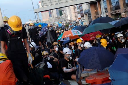 Demonstrators take cover under umbrellas as they face riot police during a protest against police violence in Hong Kong