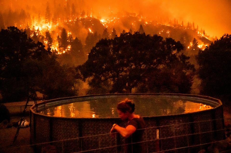 Angela Crawford leans against a fence as a wildfire called the McKinney fire burns a hillside above her home in Klamath National Forest, Calif., on Saturday, July 30, 2022 (AP)