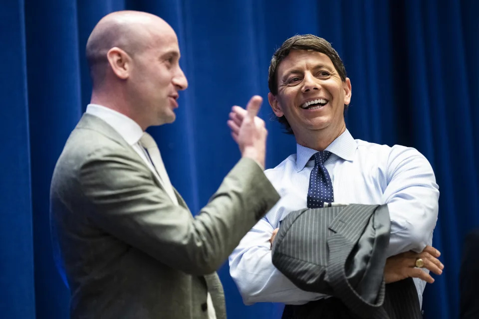 Former Trump White House aides Stephen Miller and Hogan Gidley speak to each other with smiles on their faces.