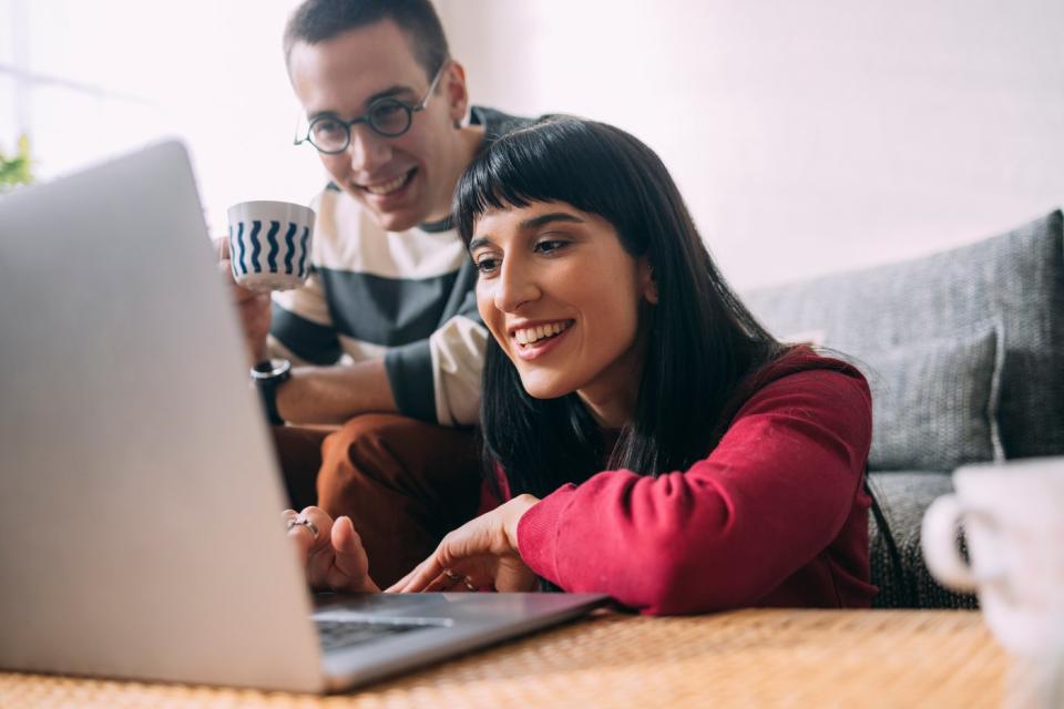 Two investors look at something on a laptop in their living room.