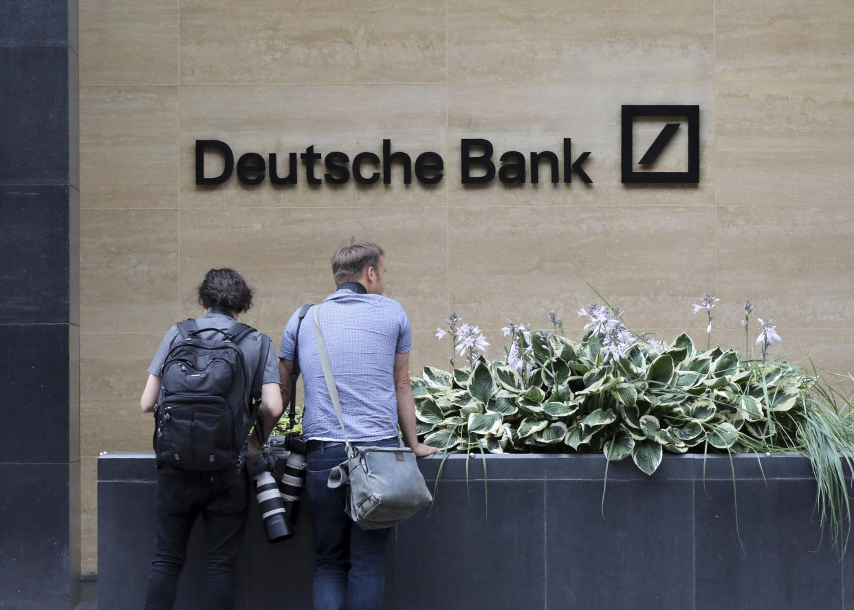 Journalists outside Deutsche Bank building in London, Monday, July, 8, 2019.  Germany's struggling Deutsche Bank says it will cut 18,000 jobs by 2022,  saying it is going “back to our roots” with a radical restructuring plan meant to focus the company on traditional strengths.(AP Photo/Natasha Livingstone)