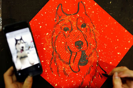 A woman draws "Fai Chun", or Chinese New Year, couplets for the upcoming Chinese Lunar New Year of the Dog, at a market in Taipei, Taiwan February 12, 2018. REUTERS/Tyrone Siu