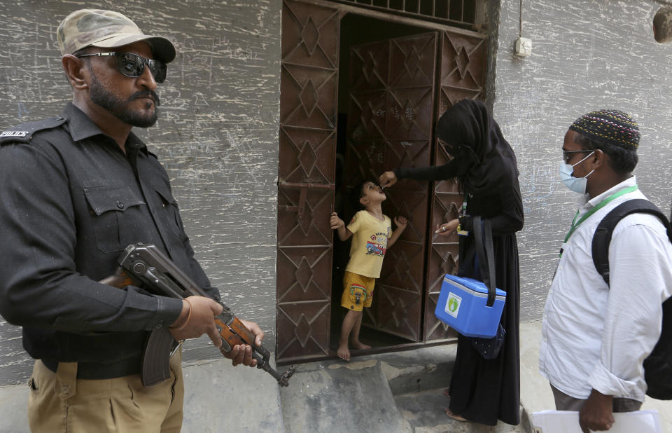 A police officer stands guard while a healthcare worker administers a polio vaccine to a child, in Karachi, Pakistan, Wednesday, June 9, 2021. Gunmen on a motorcycle Wednesday shot and killed two police officers assigned to protect polio vaccination workers in the district of Mardan in Khyber Pakhtunkhwa province, northwest Pakistan before fleeing, police said. (AP Photo/Fareed Khan)