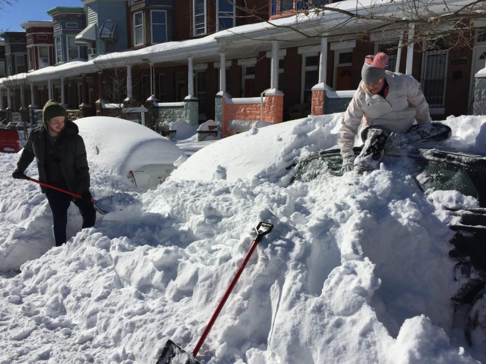 Anna Popp, 25, sits atop her snow-covered car on Guilford Avenue in Baltimore on Sunday, Jan. 24, 2016 after a storm dumped more than two feet of snow on to the city’s streets. [Juliet Linderman via AP]