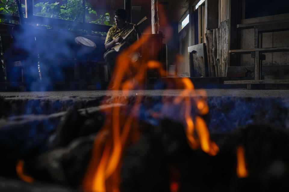Itapua Ika toca un ukelele junto a un pozo donde arden piedras volcánicas y madera, antes de colocar carne cubierta con hojas de plátano para la preparación tradicional rapanui llamada umu, en el restaurante de su familia llamado Te Ra'ai en Rapa Nui o Isla de Pascua, Chile, miércoles 23 de noviembre de 2022. (Foto AP/Esteban Félix)