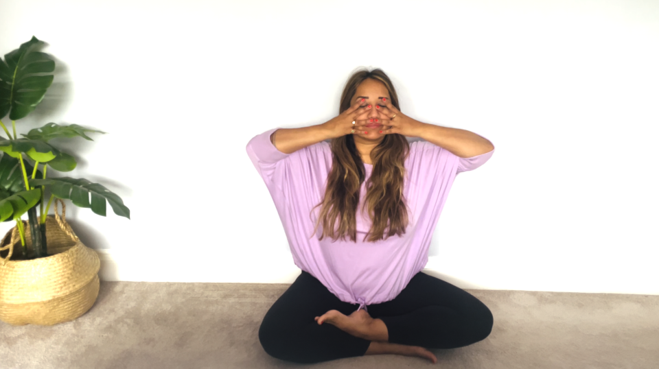 Yoga teacher Bhavini Vyas performs Brahmari breathing exercise next to a potted plant