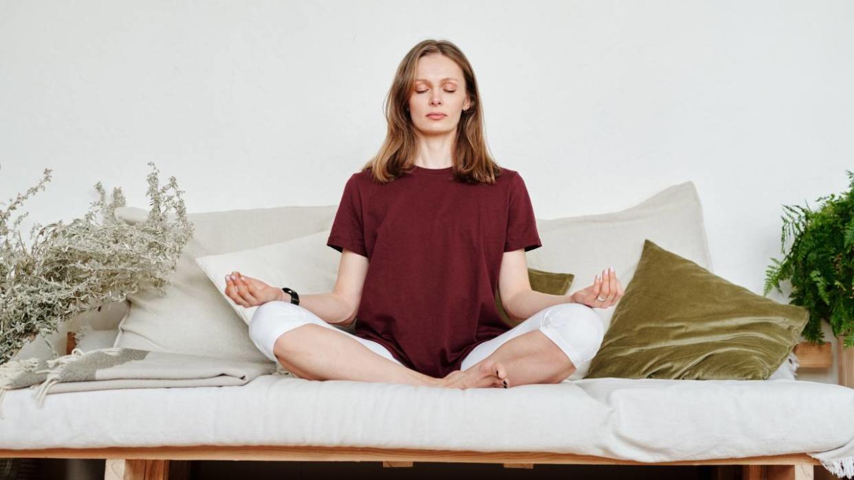  Yoga flow to boost low moods, woman sat on a sofa meditating 