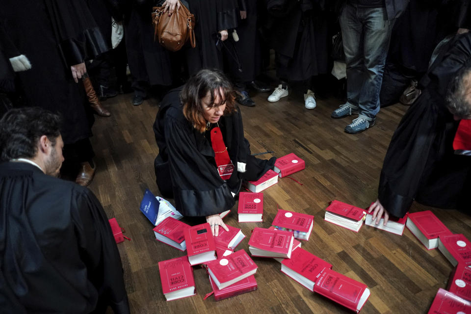 Striking lawyers angry over President Emmanuel Macron's planned overhaul of the French pension arrange legal tomes on the floor at the Lyon court house, central France, Monday Jan.13, 2020. Magistrates draped their black robes on the staircase leading to Lyon's main courthouse Monday to protest the government's plans to end the special retirement system for lawyers and others who work in the legal sector. (AP Photo/Laurent Cipriani)