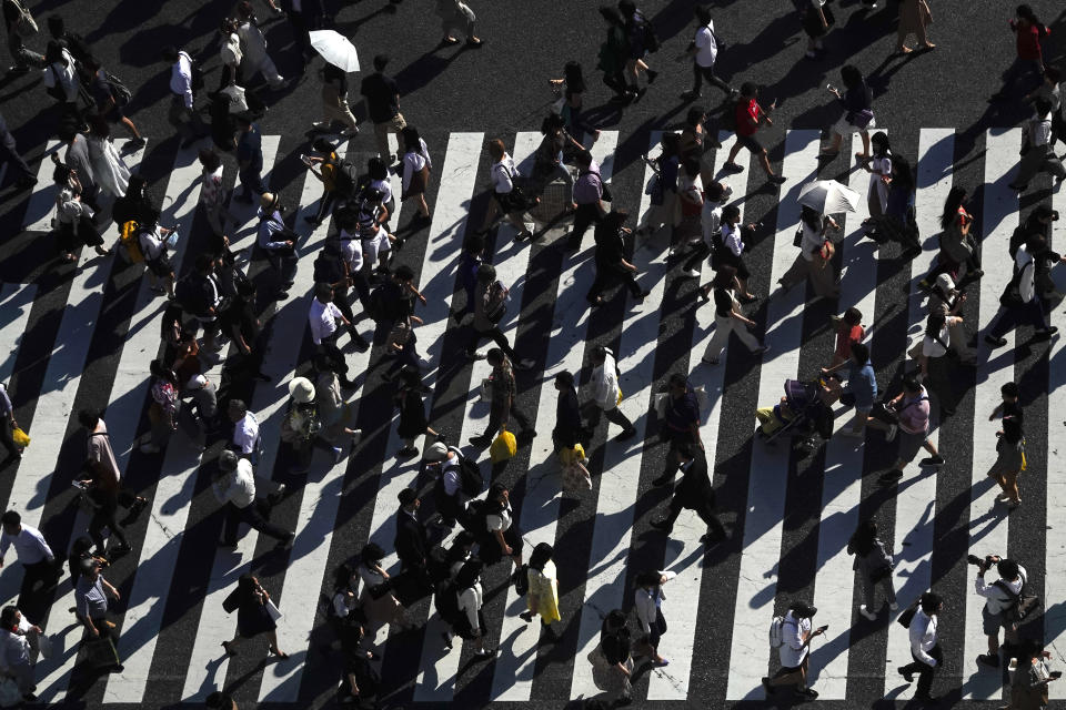 Pedestrians cast shadows as they walk across the famous Shibuya crossing Thursday, June 13, 2019, in Tokyo. It's not just a crossing. Located just outside Shibuya Station, the scramble crossing is one of the top tourist attractions in Japan. It's so famous that there's an observation deck on the rooftop of a building built to watch the crossing. During rush hour, an estimated 1000 to 2500 people cross the intersection during each traffic light change. (AP Photo/Jae C. Hong)