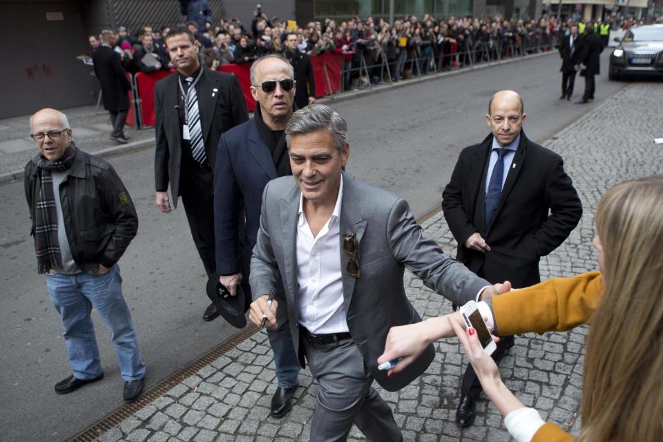 Actor George Clooney reaches out to a fan as he arrives for the photo call of the film The Monuments Men during the International Film Festival Berlinale, in Berlin, Saturday, Feb. 8, 2014. (AP Photo/Axel Schmidt)