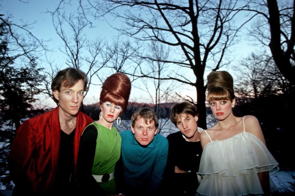 Five people in a rock band pose in front of a lake