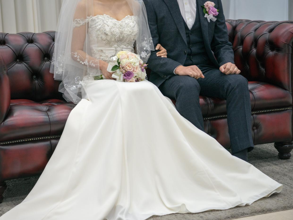 Bride in a white dress and groom in tux sitting on red sofa