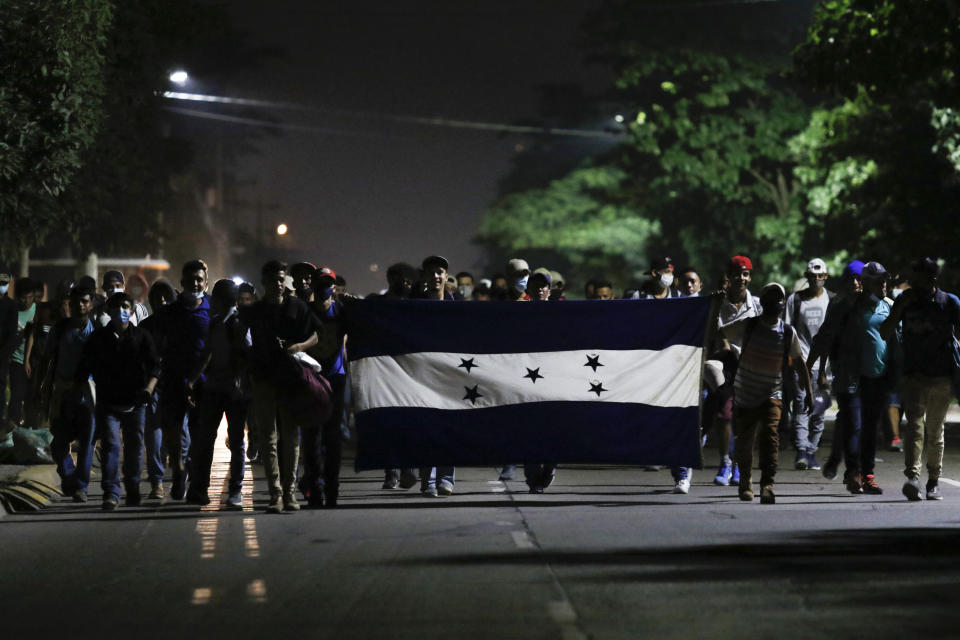 Honduran migrants trying to reach the U.S. border walk along a highway carrying their national flag as they leave San Pedro Sula, Honduras, before dawn Friday, Jan. 15, 2021. The group quickly dispersed along the heavily-trafficked highway to the border town of Agua Caliente, but estimates of their number ranged from 2,000 to more than twice that. (AP Photo/Delmer Martinez)