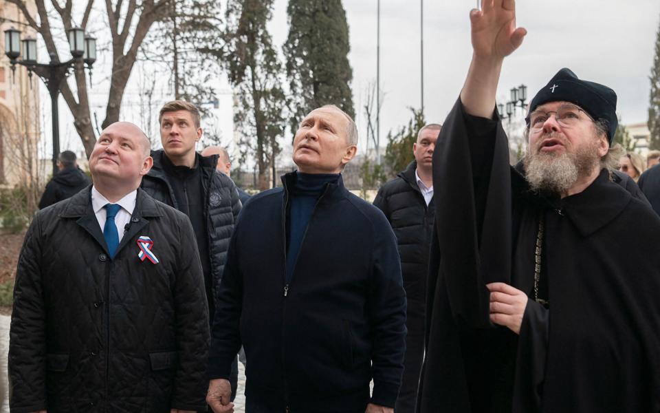 This handout photograph taken and released by the Russian presidential press office in Sevastopol on March 18, 2023, shows Russian President Vladimir Putin (L), flanked by Sevastopol Governor Mikhail Razvozhayev (C), listening to Metropolitan Tikhon Shevkunov (R), chairman of the Patriarchal Council for Culture, as he visits a children's arts-and-crafts centre, part of Chersonesos Taurica historical and archeological park on the 9th anniversary of the referendum on the state status of Crimea and Sevastopol and its reunification with Russia. (Photo by HANDOUT / Russian Presidential Press Office / AFP) / RESTRICTED TO EDITORIAL USE - MANDATORY CREDIT "AFP PHOTO / HANDOUT / RUSSIAN PRESIDENTIAL PRESS OFFICE " - NO MARKETING NO ADVERTISING CAMPAIGNS - DISTRIBUTED AS A SERVICE TO CLIENTS / Editor's note : this image is distributed by Russian state owned agency Sputnik (Photo by HANDOUT/Russian Presidential Press Offic/AFP via Getty Images) - HANDOUT/Russian Presidential Press Offic/AFP via Getty Images