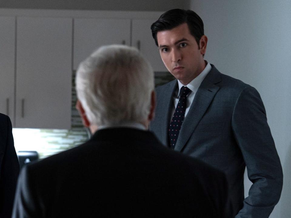 Two tall white men in suits facing a shorter, older man in an office break room.