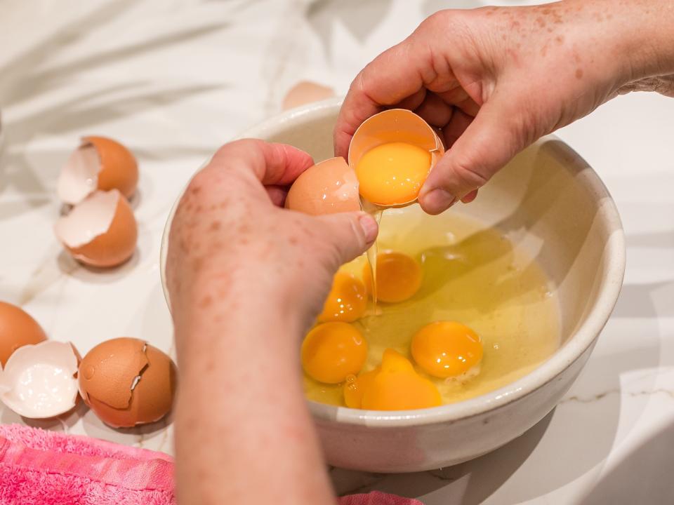 Hands cracking eggs into a bowl with already cracked eggs