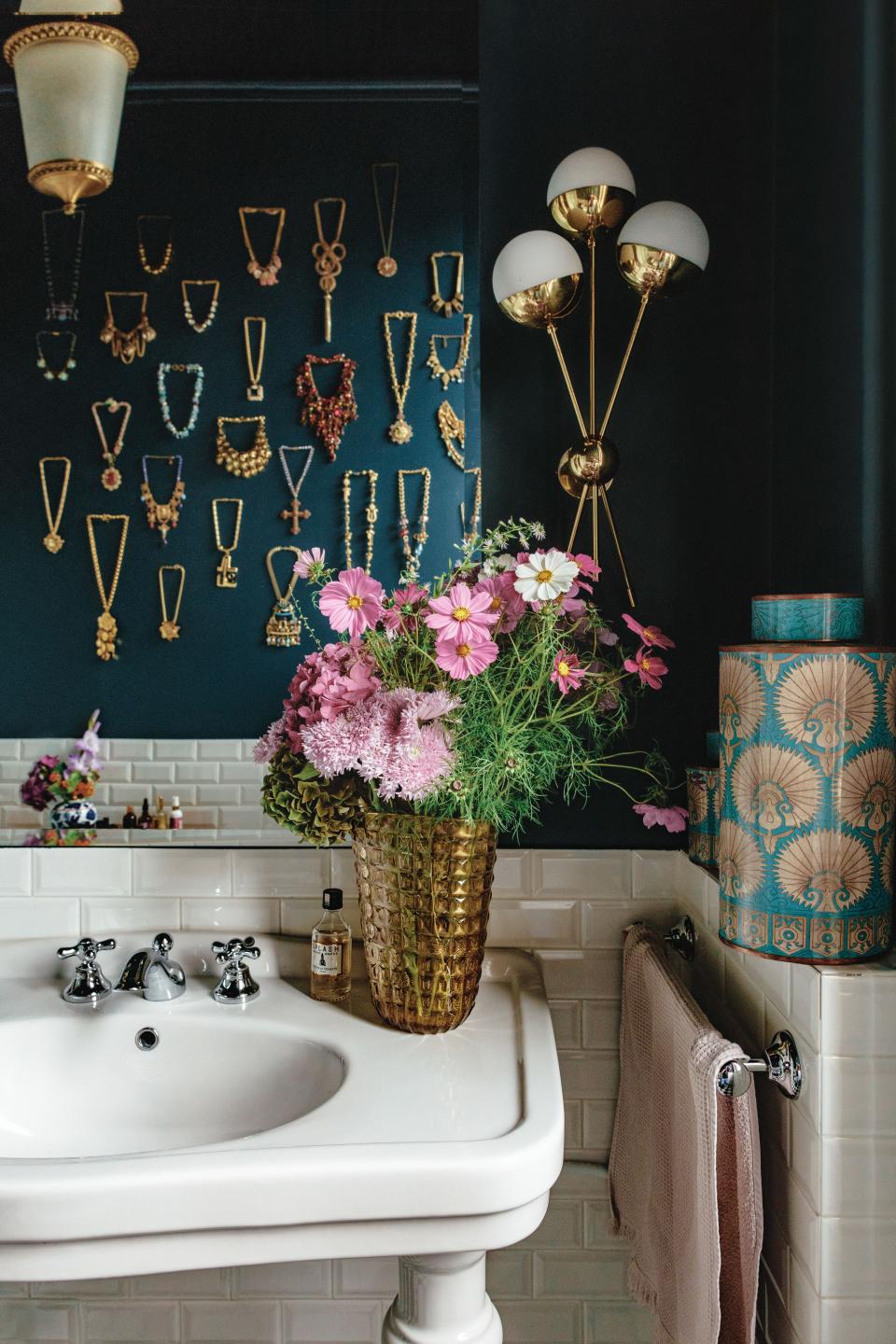 Martin’s vintage necklace collection is displayed on a bathroom wall; 1970s brass sconce.