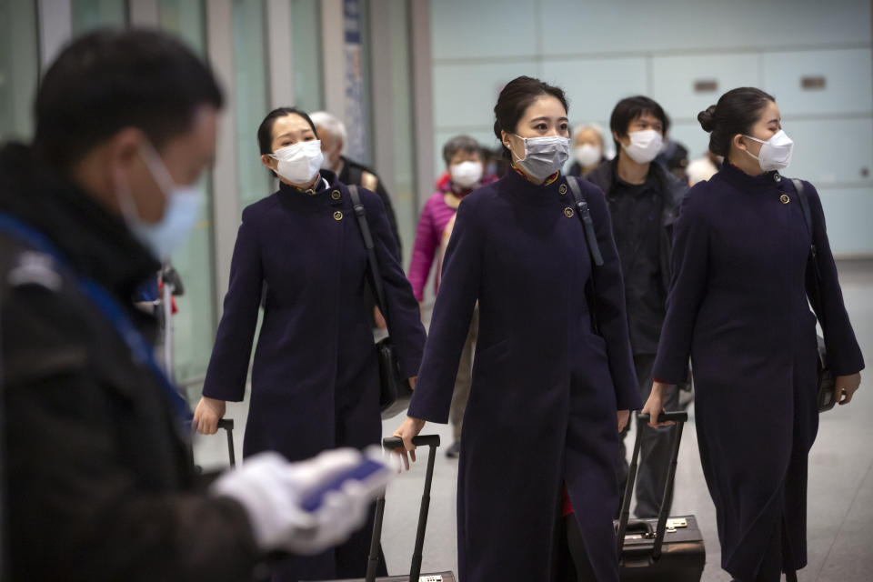 Flight crew members wearing face masks walk through the international arrivals area at Beijing Capital International Airport in Beijing, Thursday, Jan. 30, 2020. China counted 170 deaths from a new virus Thursday and more countries reported infections, including some spread locally, as foreign evacuees from China's worst-hit region returned home to medical observation and even isolation. (AP Photo/Mark Schiefelbein)